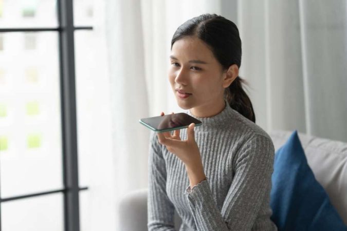 Une jeune femme utilise la commande vocale de son smartphone pour activer un générateur de voix IA.